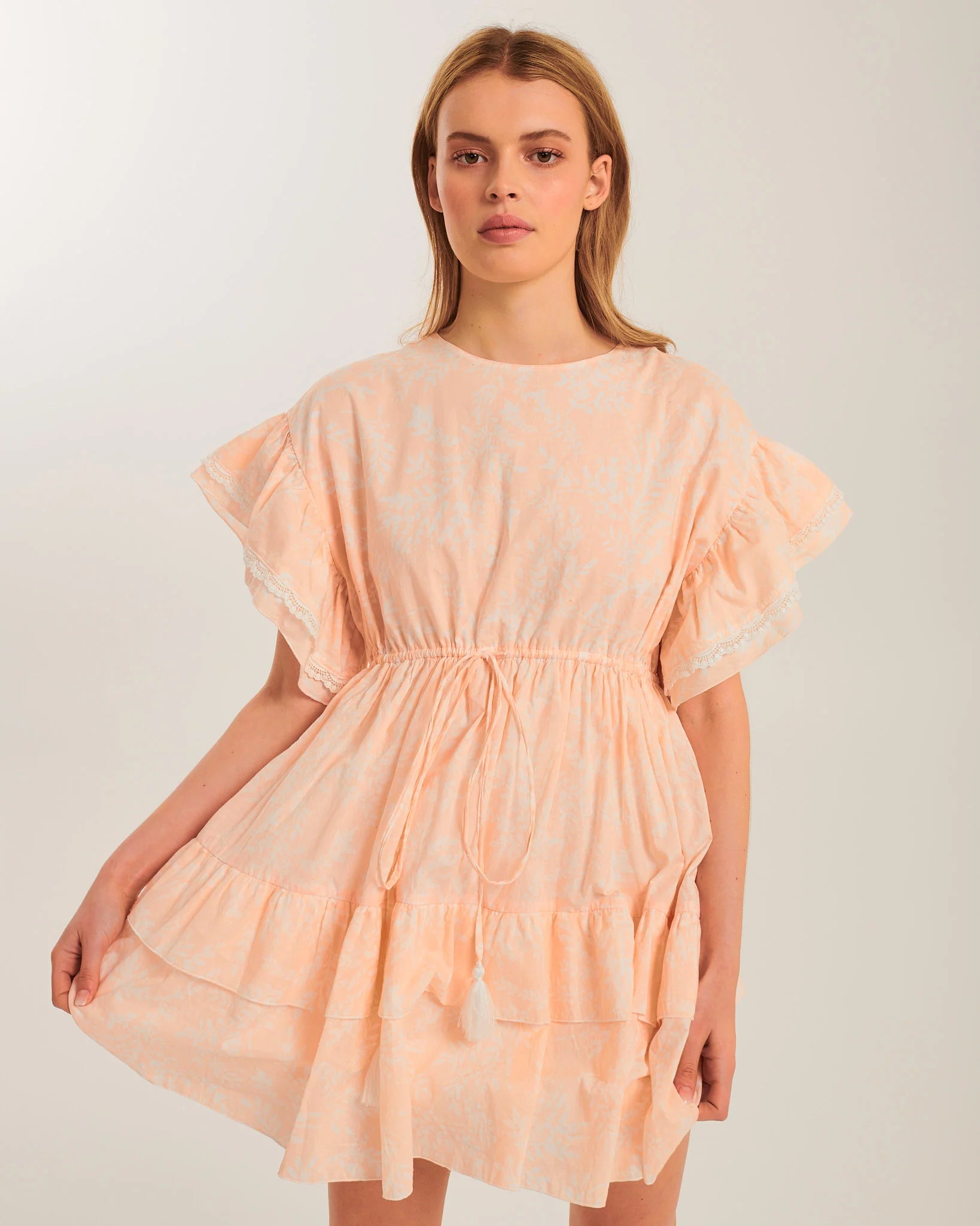 Front view of the Meadows Smock Mini Dress featuring oversized ruffled sleeves, a relaxed fit, and a drawstring waist with tassel accents | Dream Nu